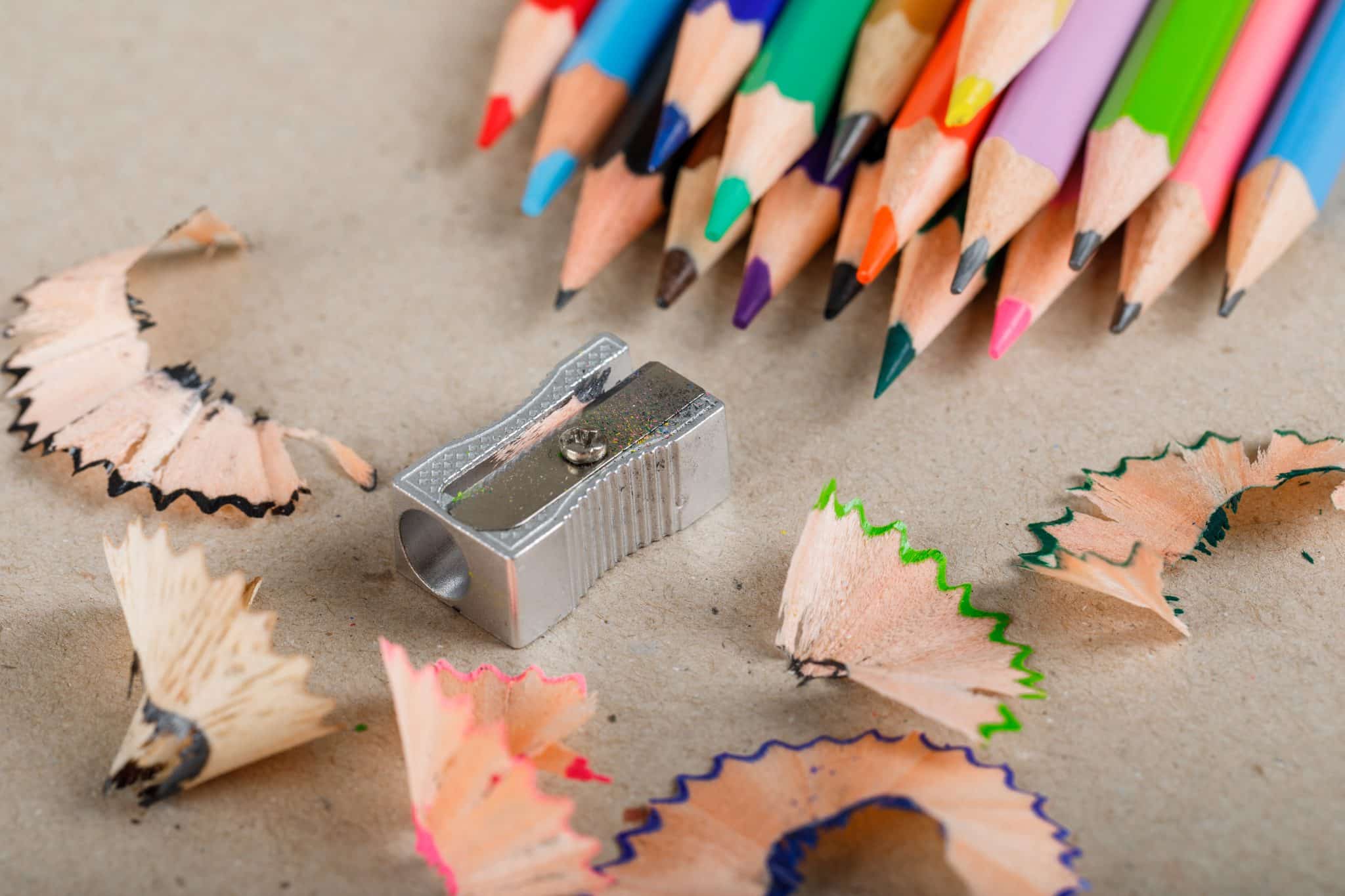 School and equipment concept with pencils, sharpener, shavings on paper background high angle view.
